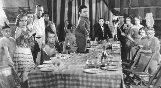 a cast of disabled performers, a dwarf man in a suit is standing on the table