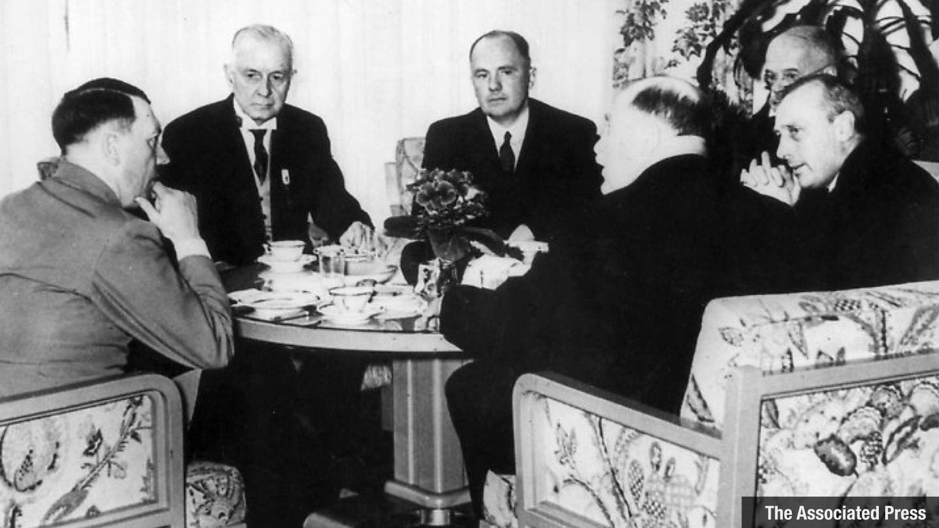 A black and white photo of Hitler meeting with Thomas Watson (CEO of IBM) and other business men around a table with an expensive looking tea set placed on it